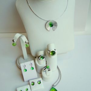 Silbernes Schmuckset mit leuchtend grünen Steinen: Halskette mit rundem Anhänger, mehrere Ringe, Ohrhänger und Ohrstecker, dazu ein zusätzlicher grüner Kettenanhänger.