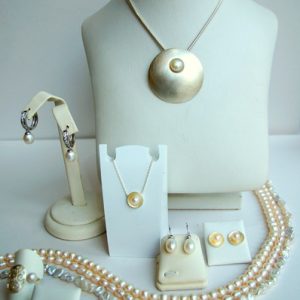 Elegantes Perlen-Schmuckset mit großem Anhänger, passenden Ohrringen, Ringen und mehreren Perlenketten, präsentiert auf weißen Schmuckdisplays.