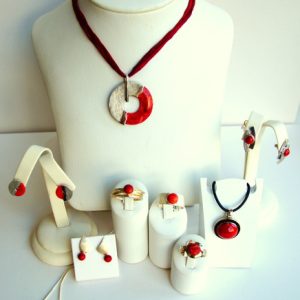Schmuckarrangement mit roten Stein-Elementen, bestehend aus Halsketten, Ohrringen, Ringen und einem Armband, auf weißen Ständern präsentiert.