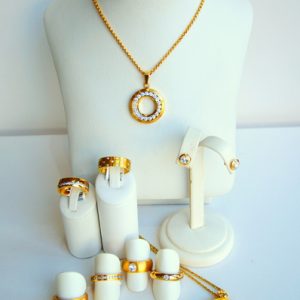 Goldfarbenes Schmuckset mit funkelnden weißen Steinen: eine runde Anhängerkette, Ohrstecker, mehrere Ringe sowie ein zweiter runder Anhänger mit filigranem Baummotiv